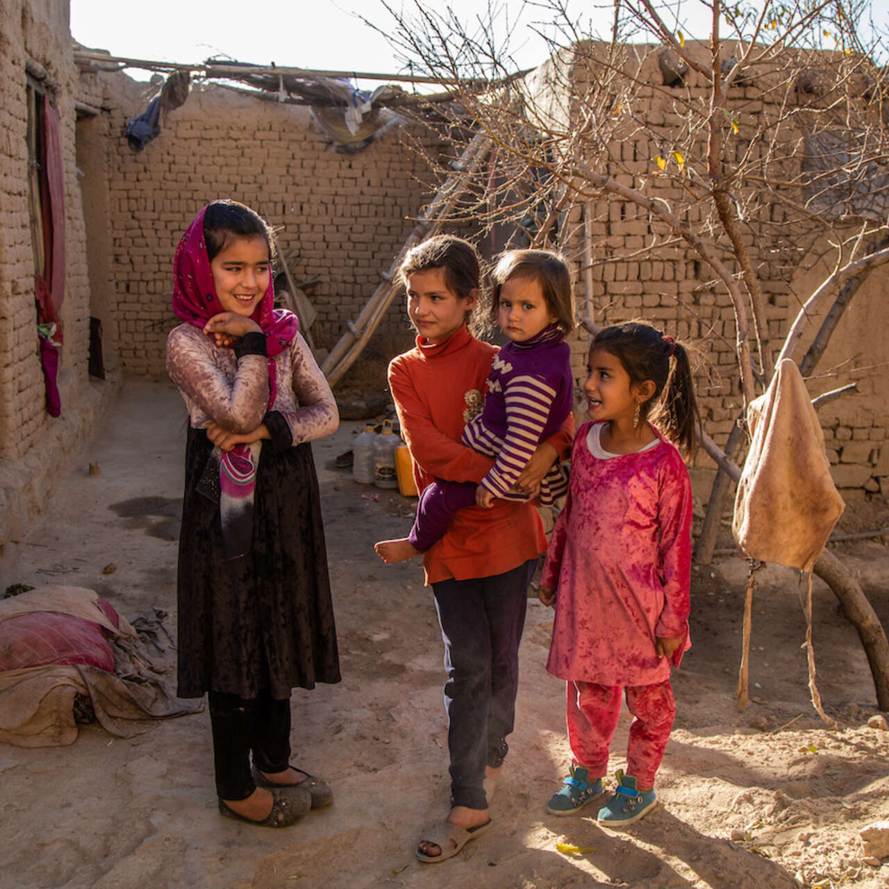 Fyra flickor står tillsammans framför ett enkelt hus i Afghanistan, där det pågår en humanitär kris.